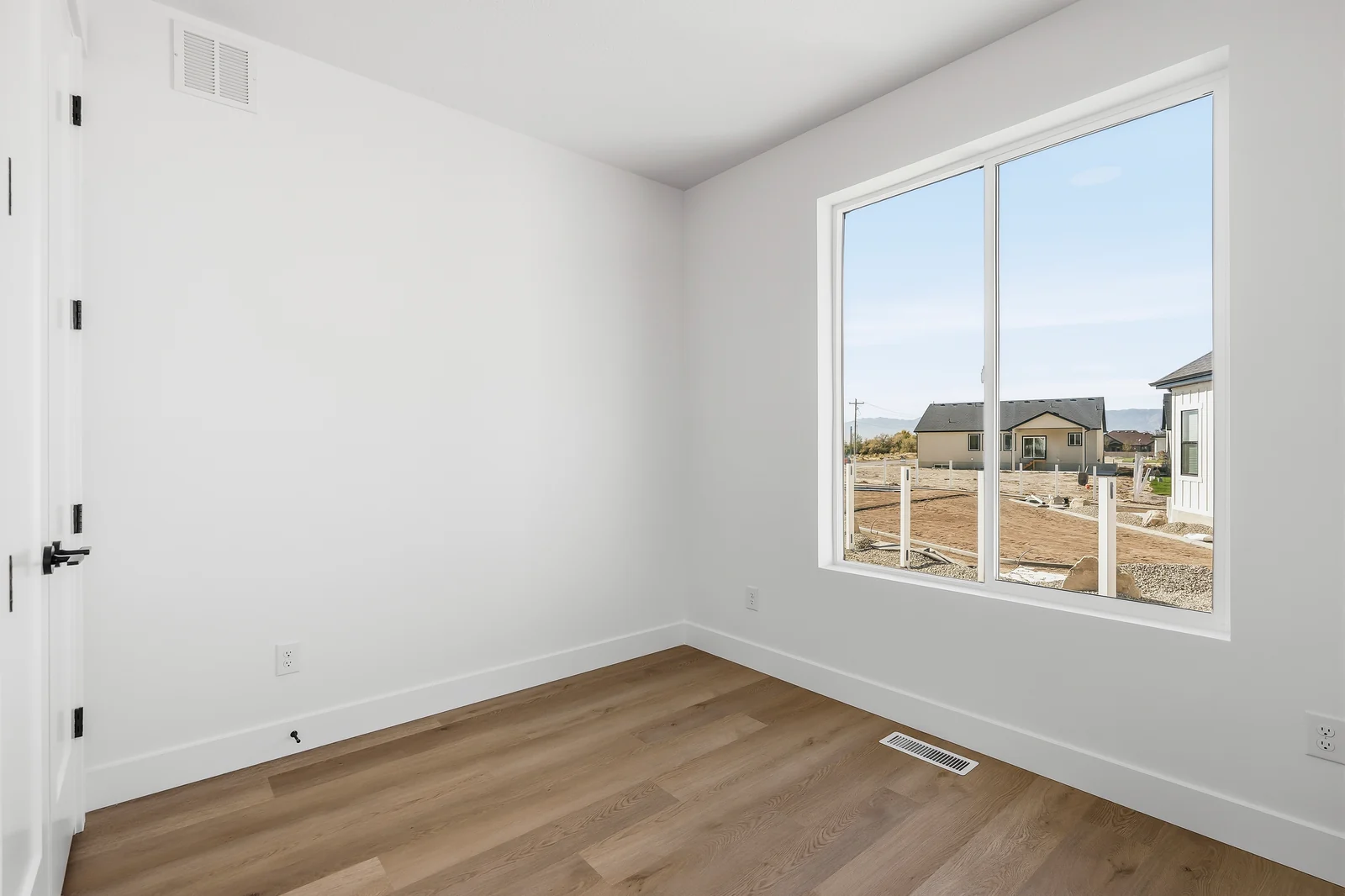 Bright empty bedroom with wood-look flooring, white walls, and a large neighborhood-facing window at Chestnut MW311, Stansbury Park.