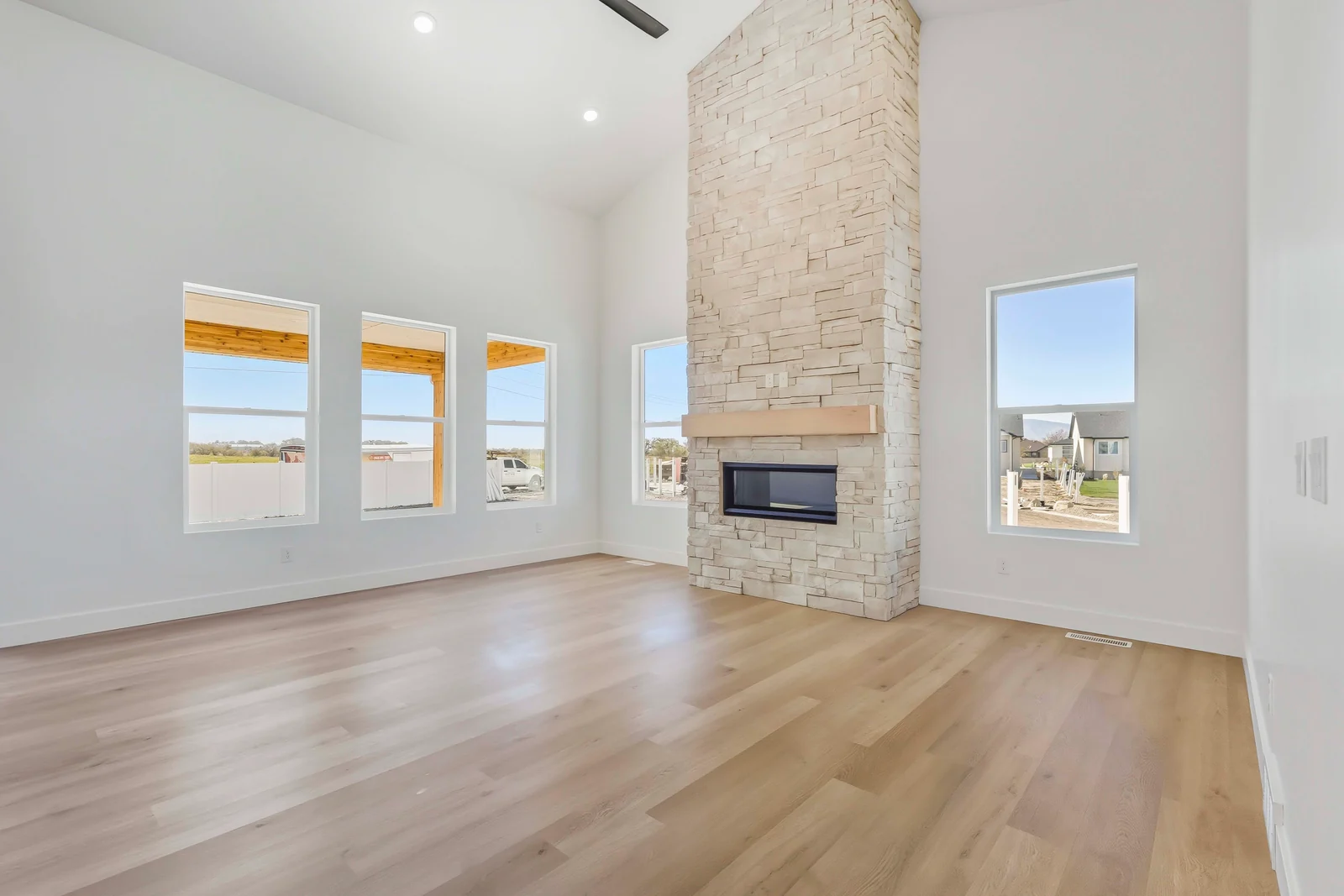 Great room with high ceiling, stone fireplace, wood-look flooring, and rows of bright windows at Chestnut MW311, Stansbury Park.