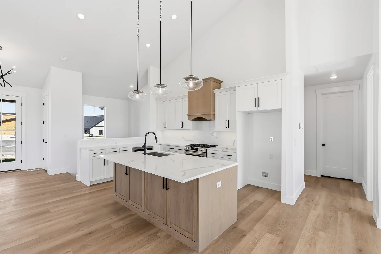 White kitchen with large island, dark hardware, pendant lights, pantry door, and wood-look flooring at Chestnut MW311, Stansbury Park.