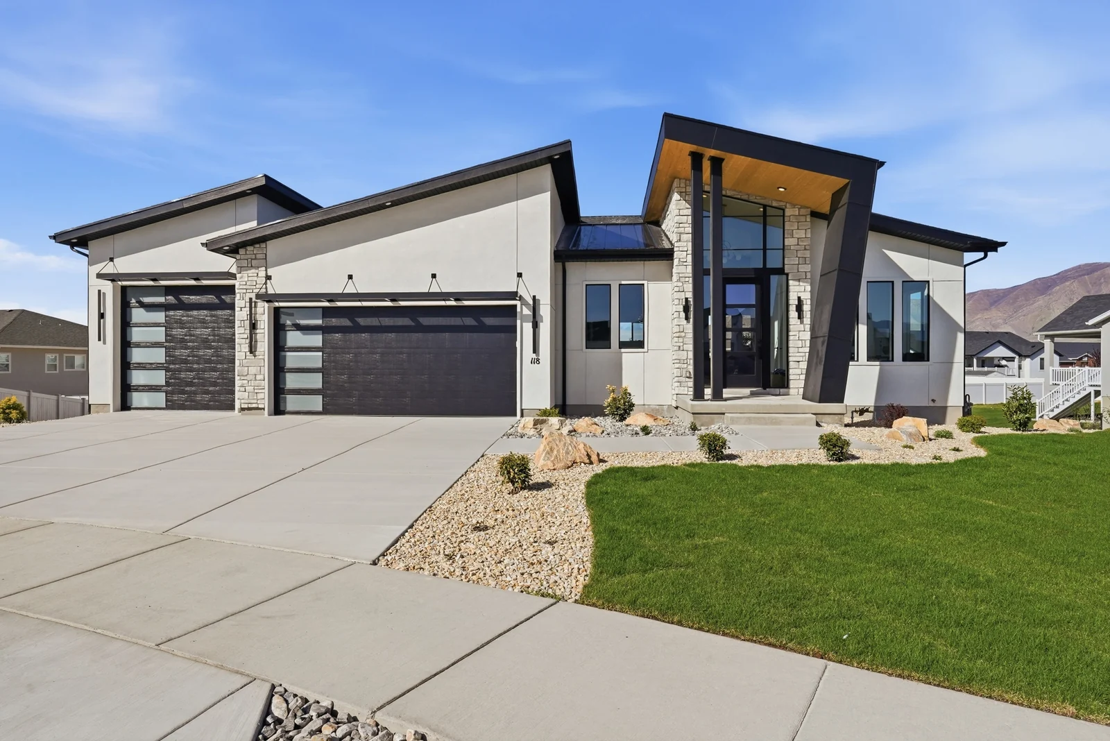 Daytime front exterior with dark garage doors, covered entry, concrete drive, and lawn in Chestnut Modern MW302, Stansbury Park.