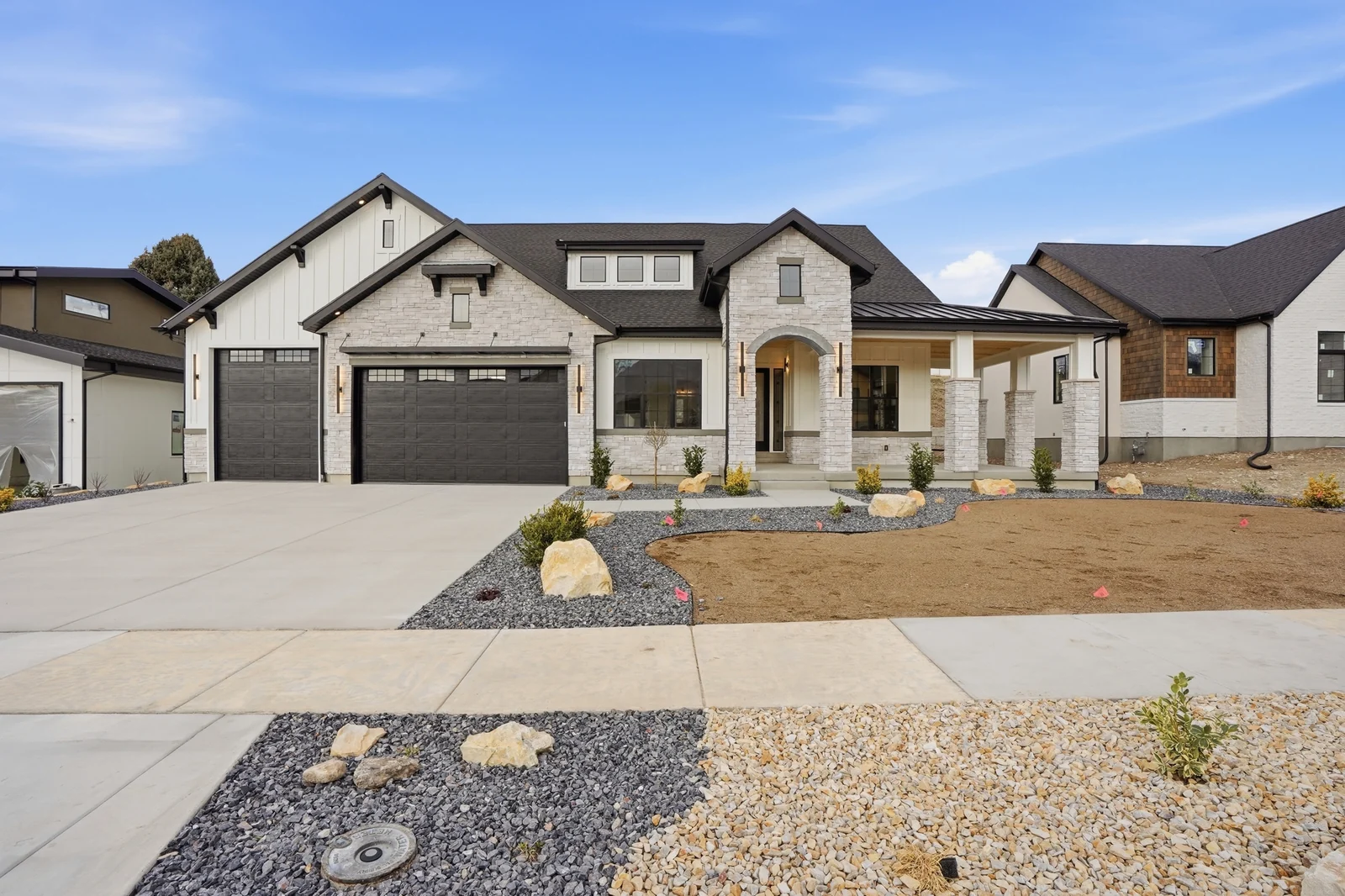Frontal view of the stone-and-siding facade, dark garage doors, and concrete driveway in Olympic BH08, American Fork.