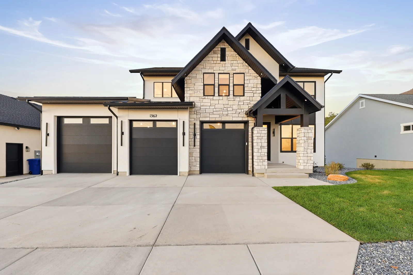Front exterior shows a light facade, dark gables, three garage doors, driveway, and lawn in Hawthorne Farmhouse, Ogden.