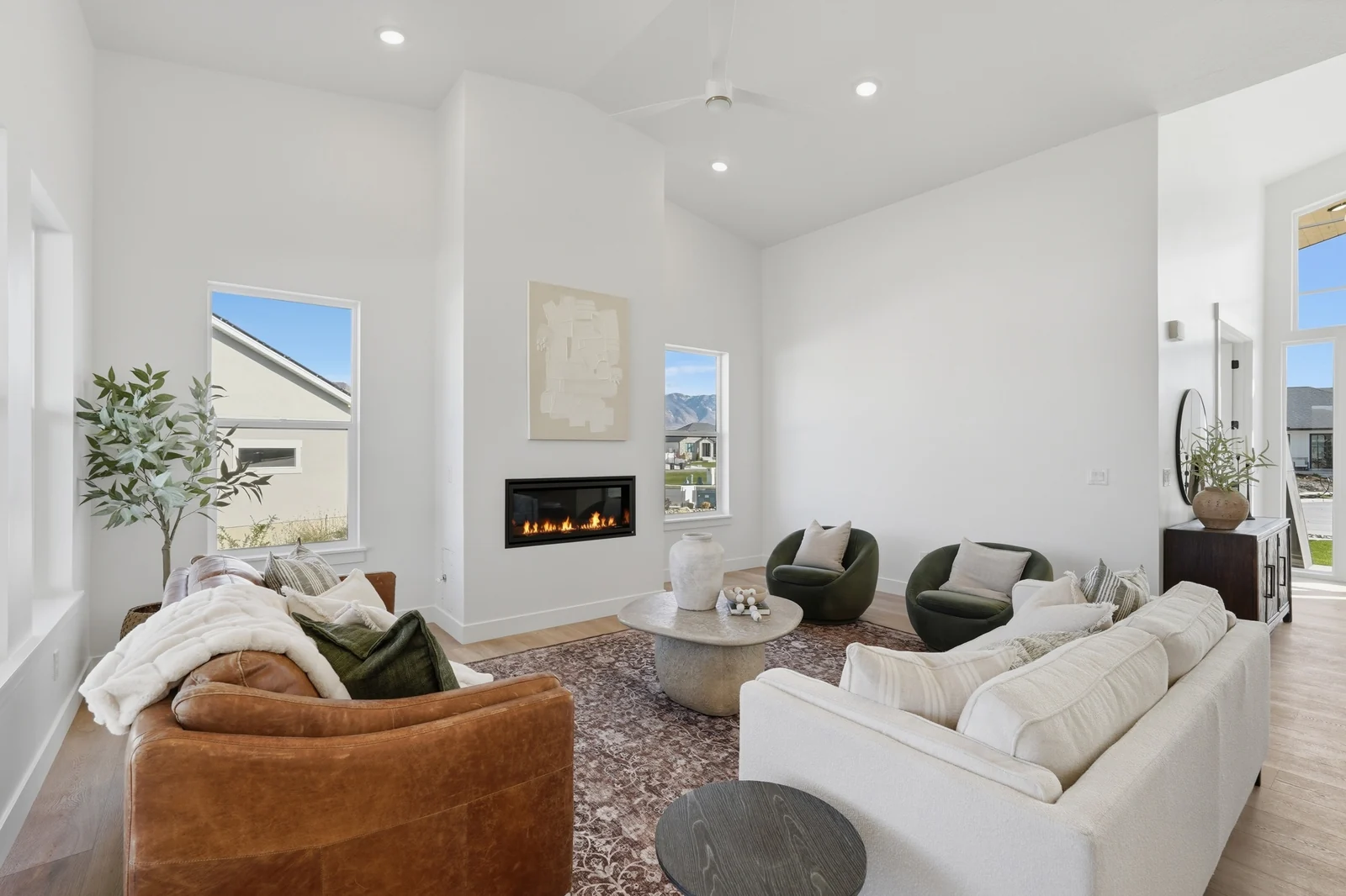 Bright living room with seating, fireplace, tall windows, and open sightline toward the kitchen in Chestnut Modern MW302, Stansbury Park.