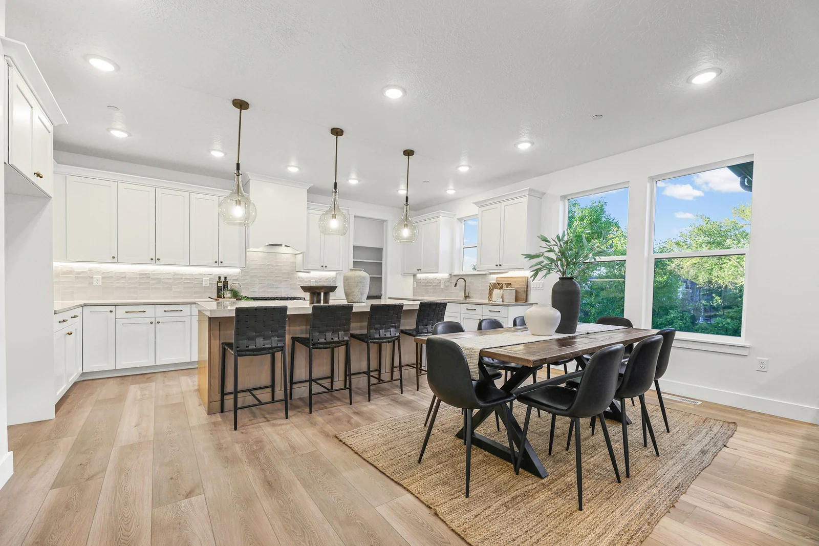 Bright kitchen with white cabinets, wood island, dining table, and large windows in Hawthorne Farmhouse, Ogden.
