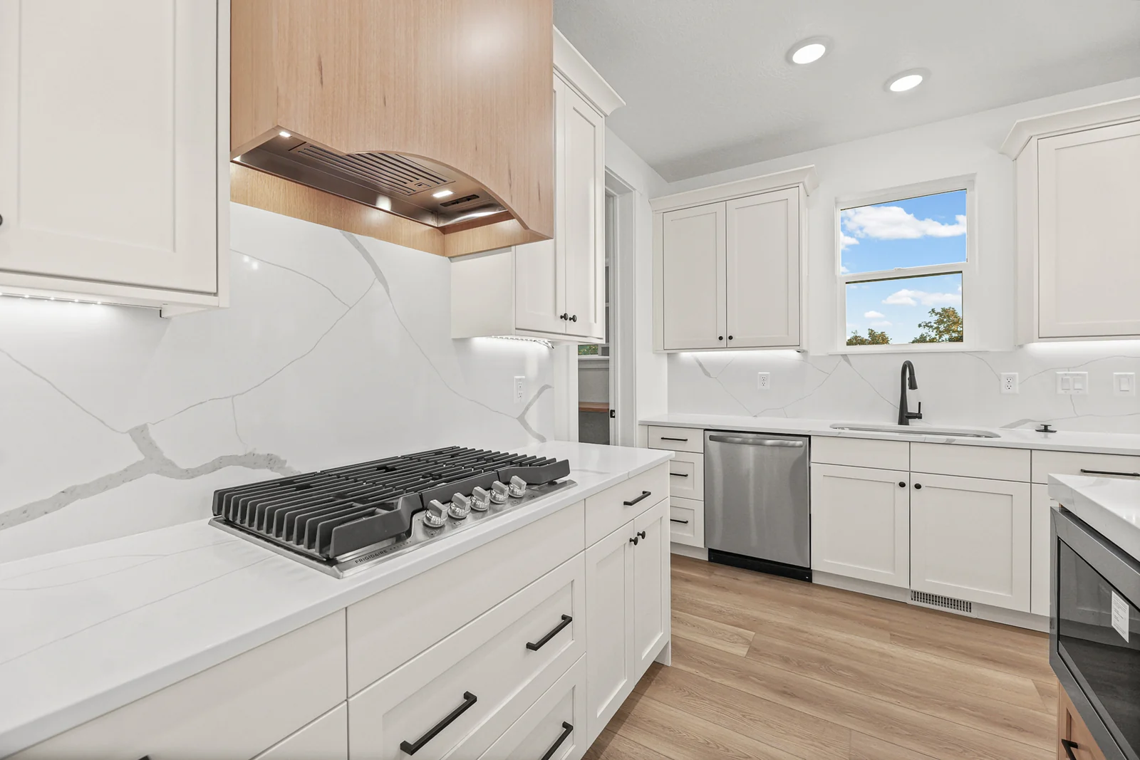 White kitchen with stainless gas range, marble-look backsplash, white cabinets, and wood-look flooring in Hawthorne Modern, Ogden.