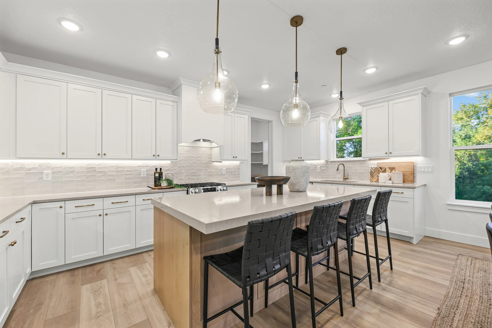White kitchen cabinetry surrounds a wood-base island with seating and pendant lights in Hawthorne Farmhouse, Ogden.