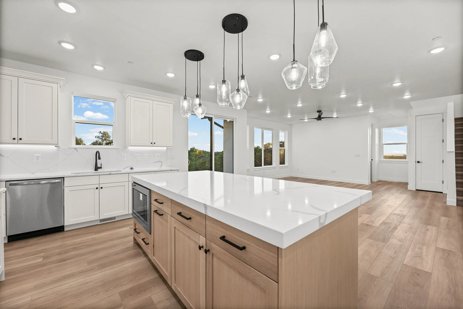 Kitchen island with wood cabinetry, white countertop, pendant lights, and adjacent dining space in Hawthorne Modern, Ogden.