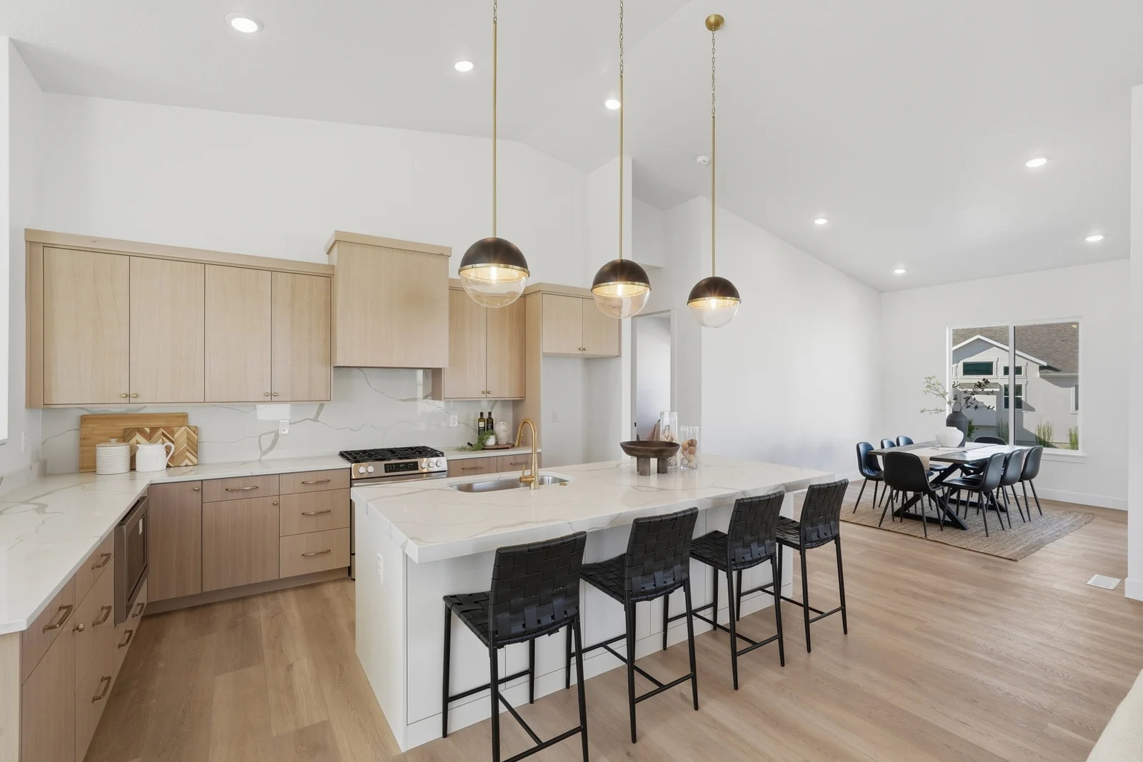 Open kitchen with pale wood cabinetry, white island, pendant lights, and black stools in Chestnut Modern MW302, Stansbury Park.