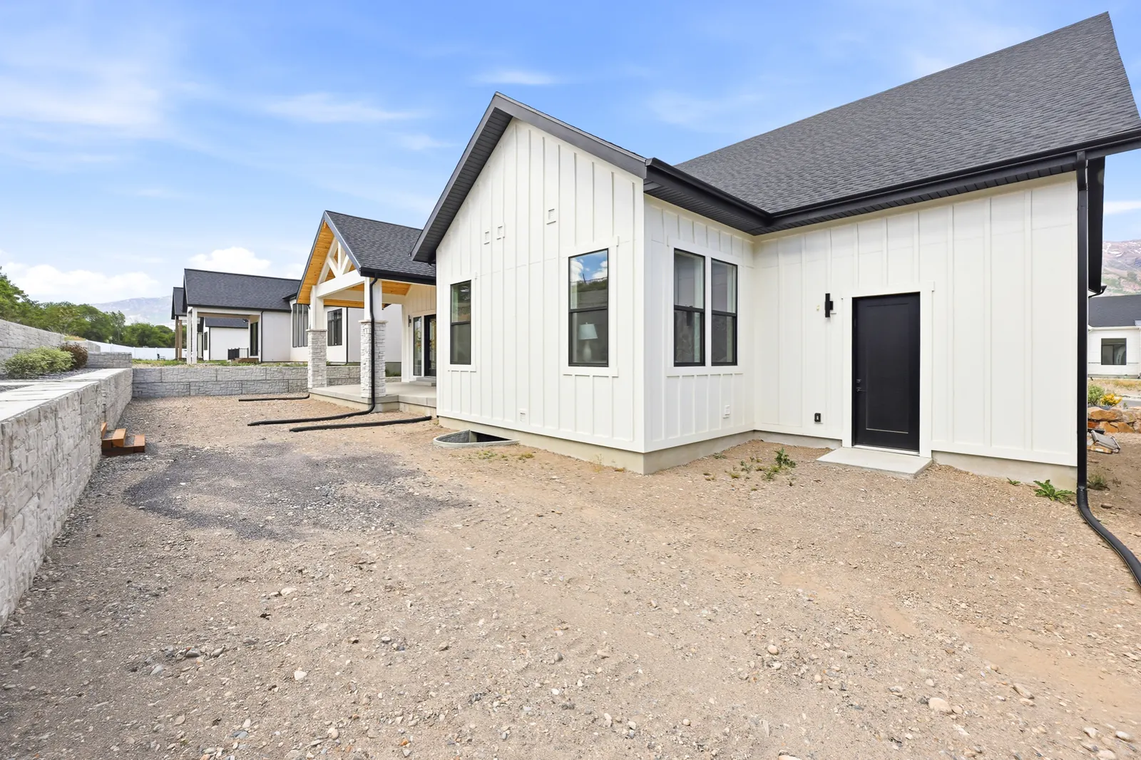 Side view of the white exterior, driveway edge, and unfinished ground beside neighboring homes in Olympic BH08, American Fork.