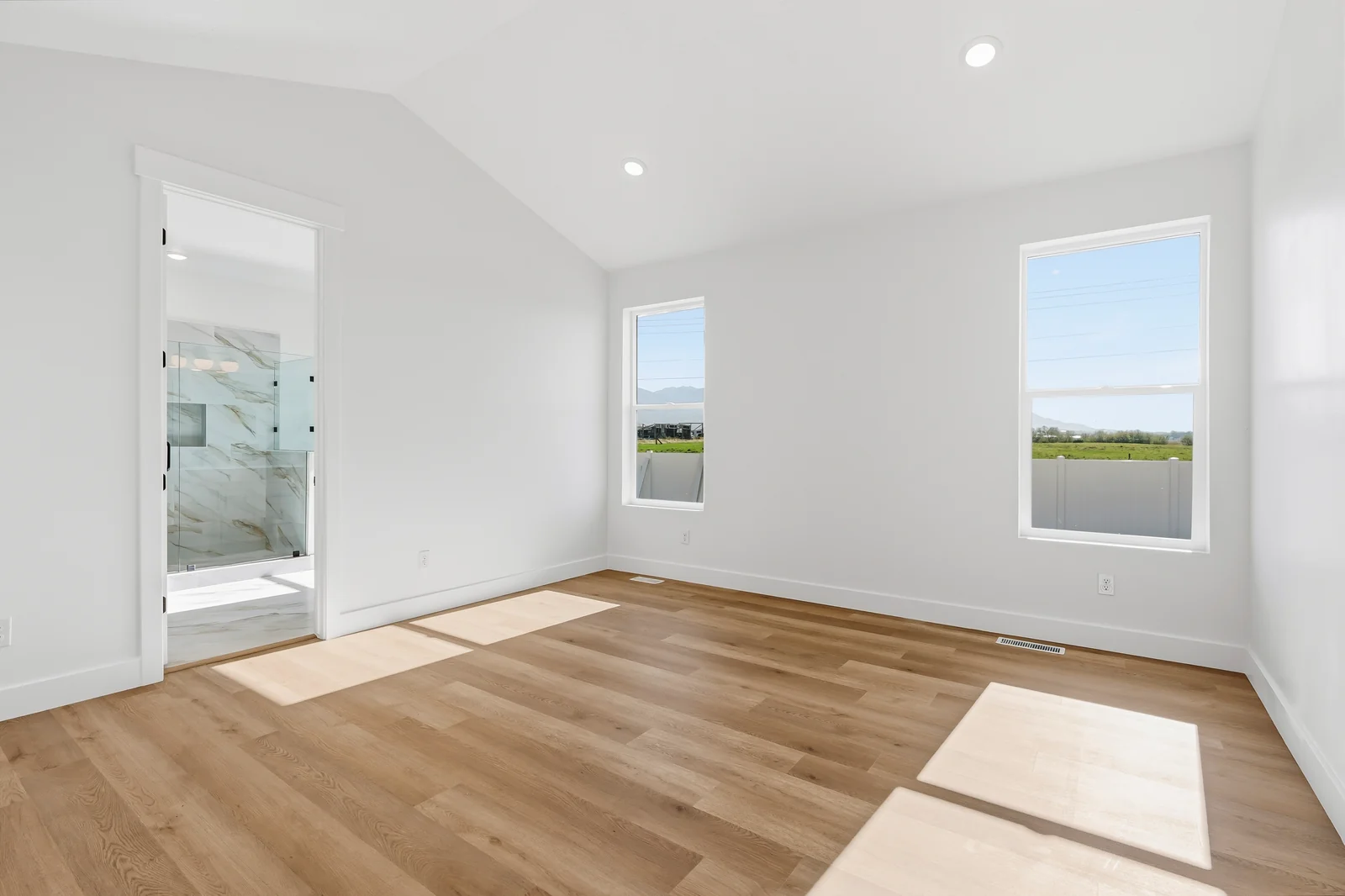 Spacious empty bedroom with two windows, wood-look flooring, and an open doorway toward the bathroom at Chestnut MW311, Stansbury Park.