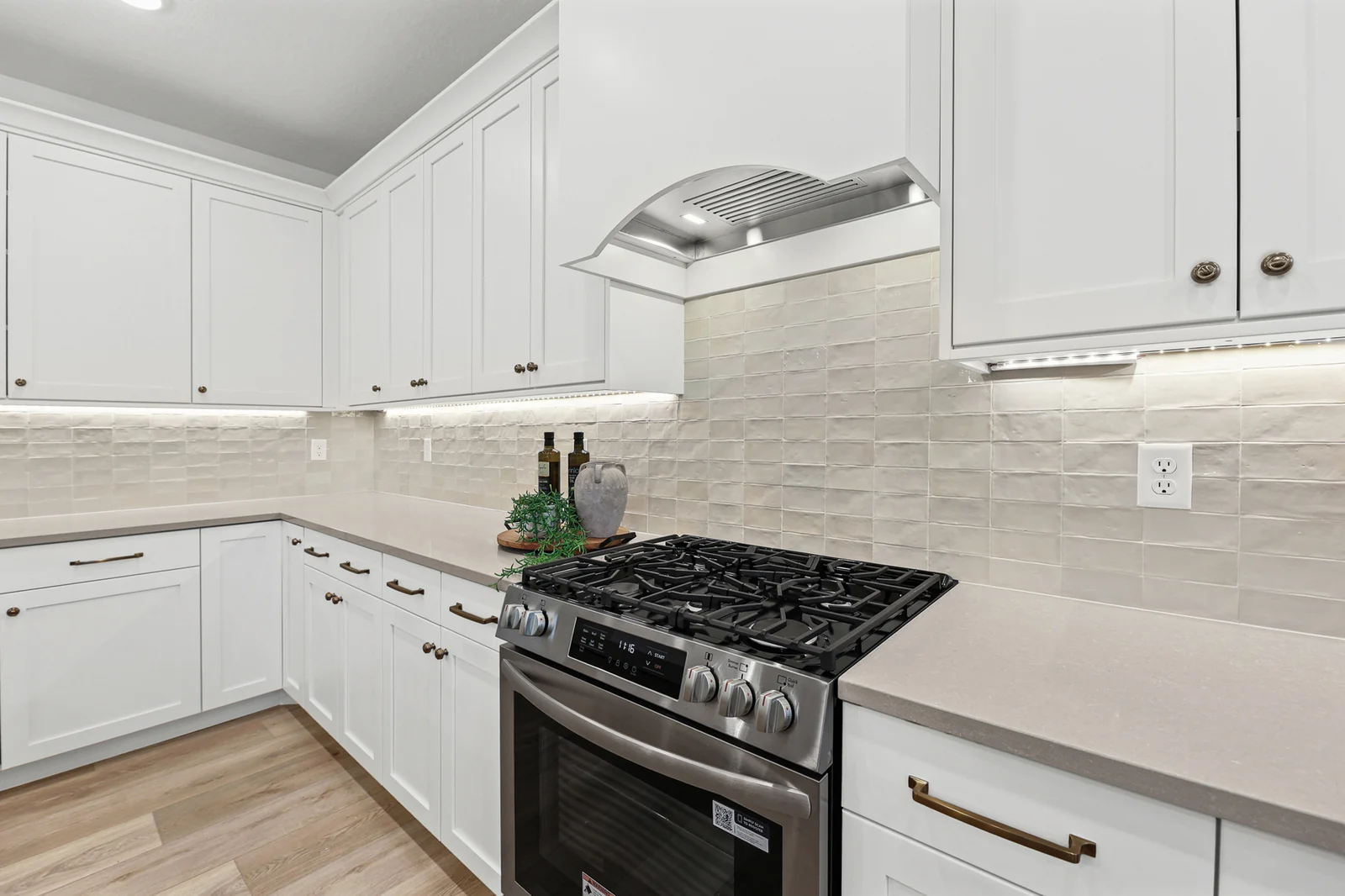 Black range sits beneath a stainless hood, surrounded by white cabinets and tile backsplash in Hawthorne Farmhouse, Ogden.