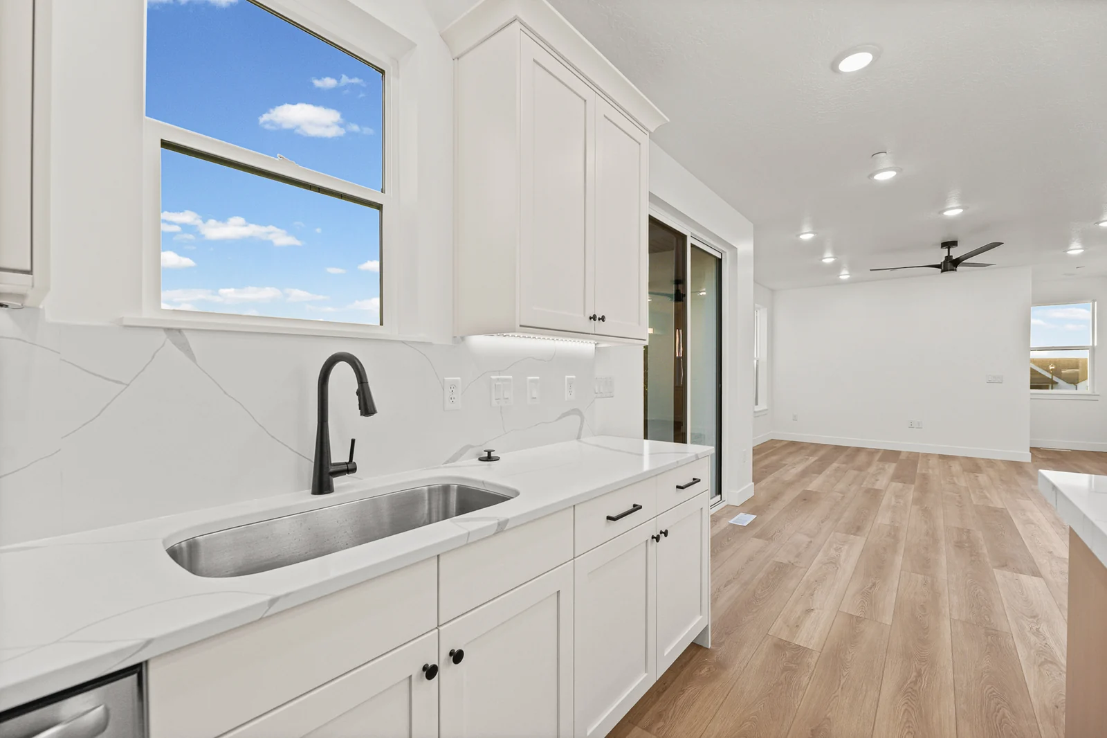 Kitchen sink beneath a large window with white cabinetry and an open living area beyond in Hawthorne Modern, Ogden.