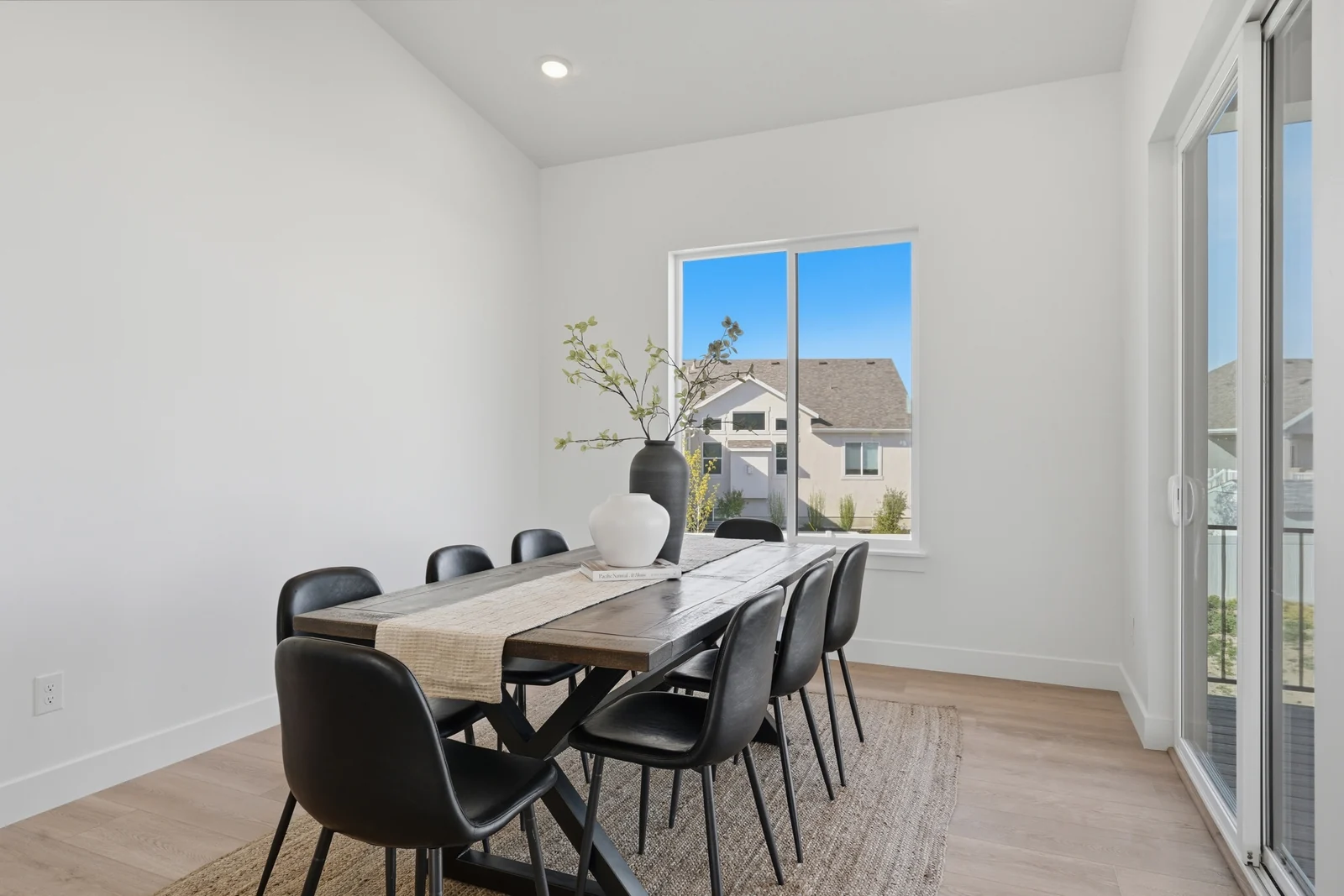 Dining table with black chairs beside large glass doors opening to the covered patio in Chestnut Modern MW302, Stansbury Park.