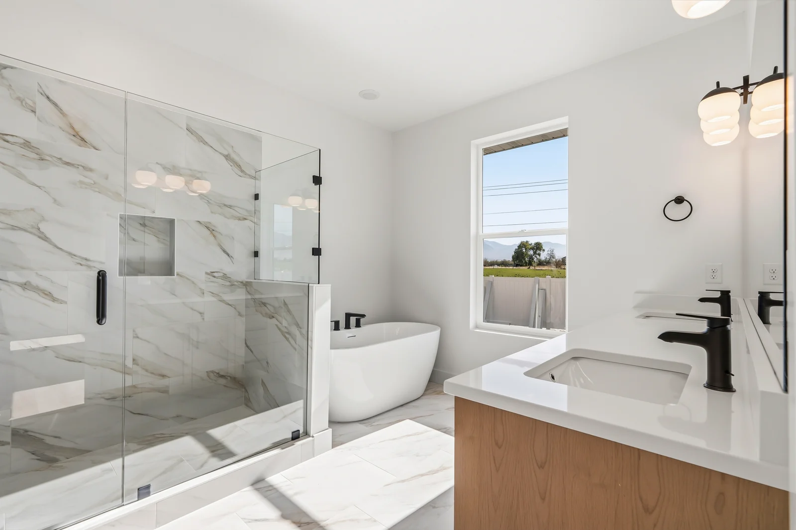 Bright bathroom featuring a freestanding tub, glass shower, marble-look tile, window, and vanity at Chestnut MW311, Stansbury Park.