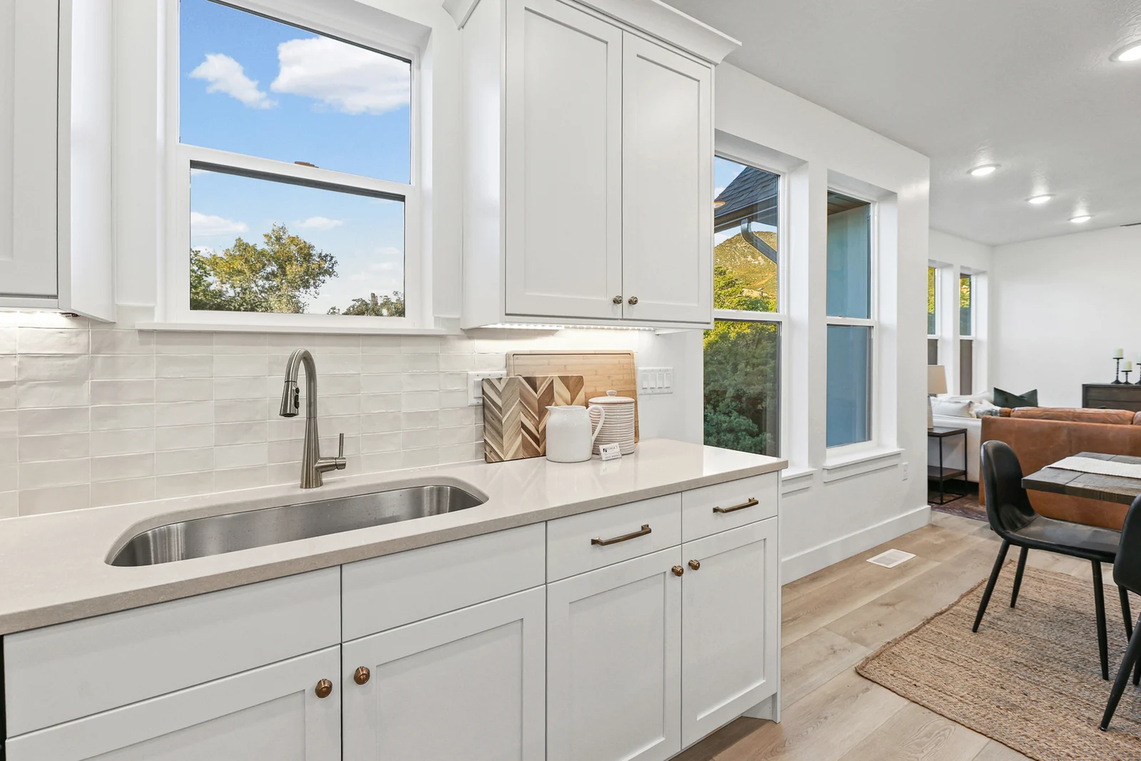 Kitchen sink beneath a window overlooks white cabinetry, the island, and dining seating in Hawthorne Farmhouse, Ogden.