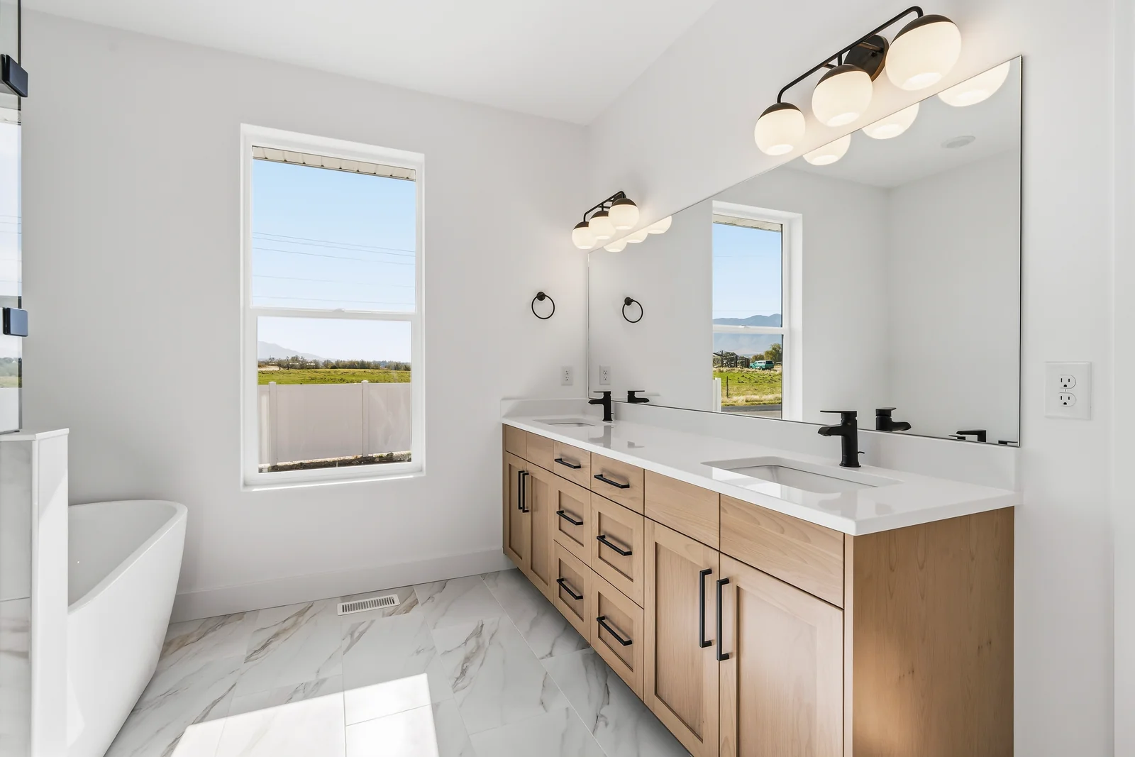 Double-sink wood vanity with black fixtures, marble-look counter, and framed mirror beside the tub at Chestnut MW311, Stansbury Park.