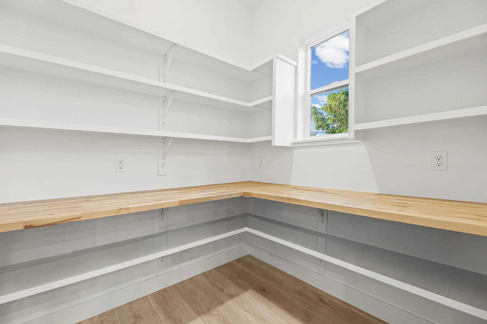 Walk-in pantry displays wraparound white shelves, wood countertops, and light wood flooring in Hawthorne Farmhouse, Ogden.