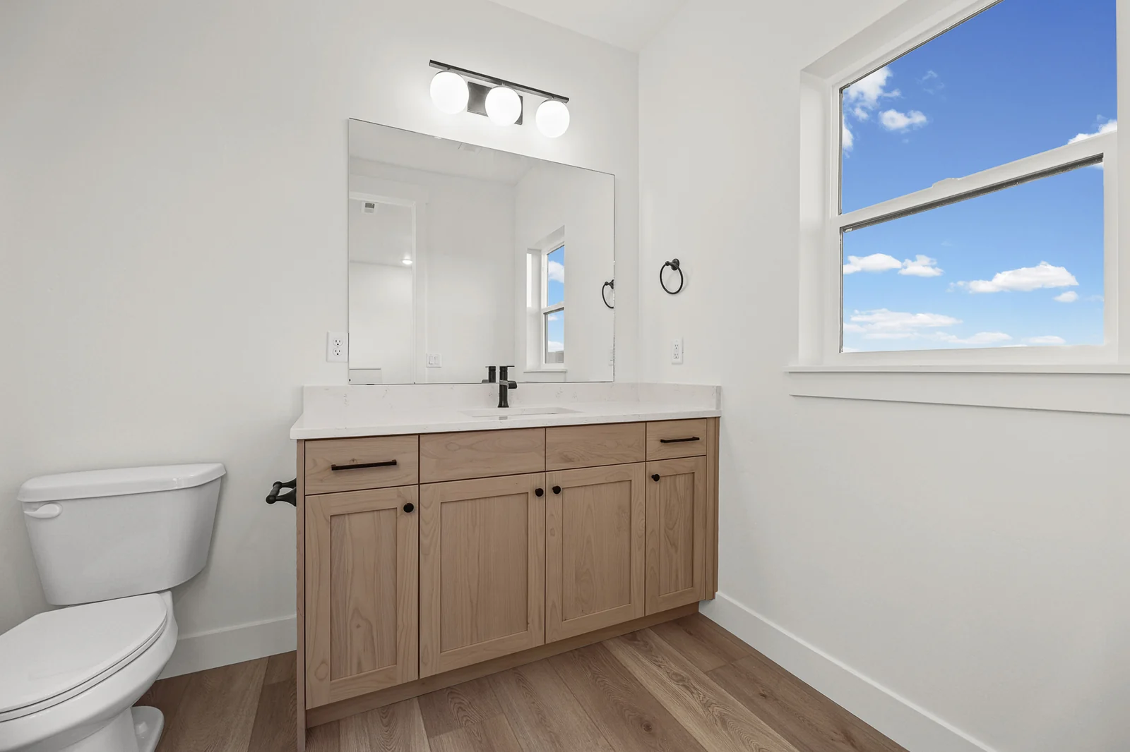 Bathroom with wood vanity, white countertop, black fixtures, toilet, and window in Hawthorne Modern, Ogden.