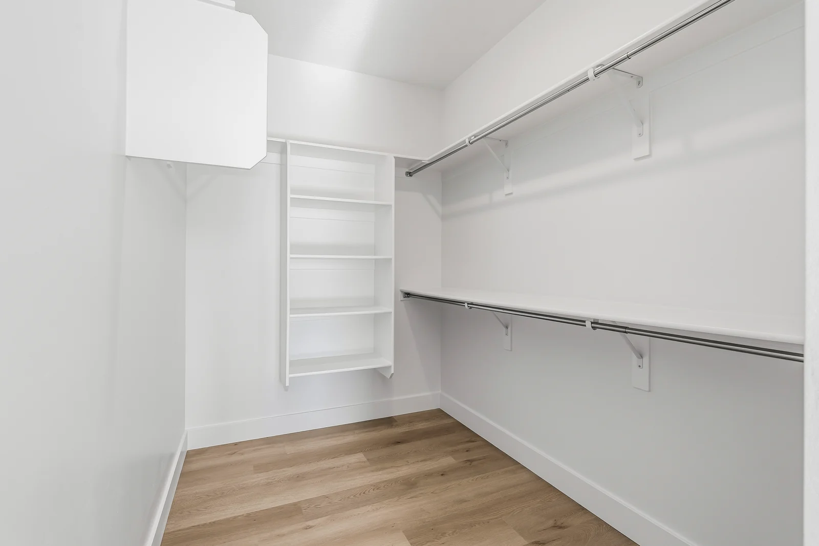 Walk-in closet with built-in white shelving, hanging rods, wood-look flooring, and overhead light at Chestnut MW311, Stansbury Park.