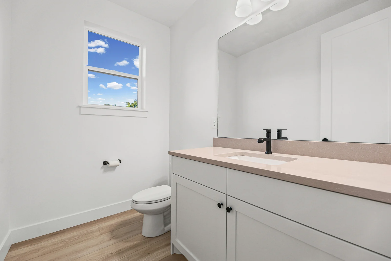 Bathroom includes a pale vanity, wood-toned countertop, black faucet, toilet, and window in Hawthorne Farmhouse, Ogden.