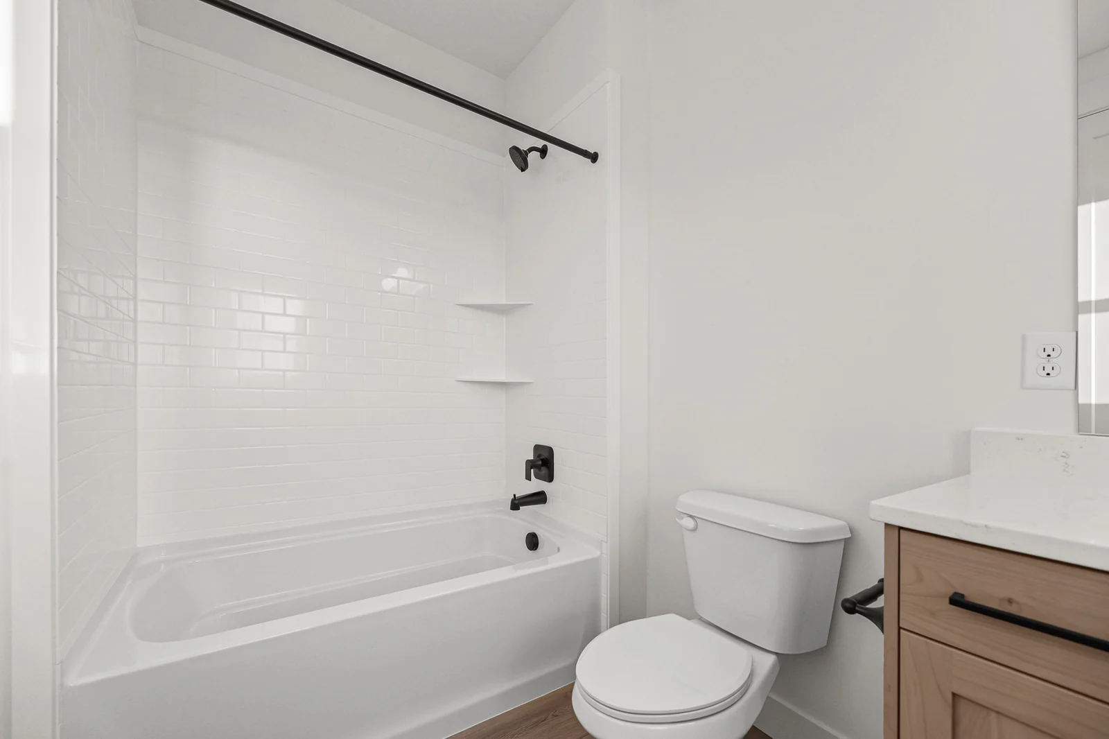 Bathroom with white tub-shower surround, black curtain rod, vanity edge, and toilet in Hawthorne Modern, Ogden.