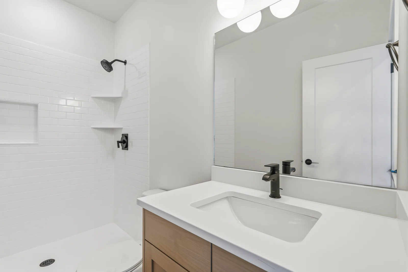 Bathroom vanity with black faucet, mirrored cabinet, white shower surround, and wood-look flooring at Chestnut MW311, Stansbury Park.