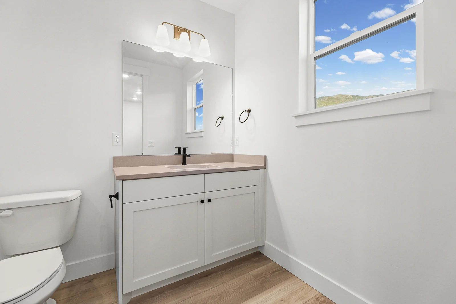 Bathroom vanity with mirrored cabinet, black faucet, toilet, and bright window in Hawthorne Farmhouse, Ogden.