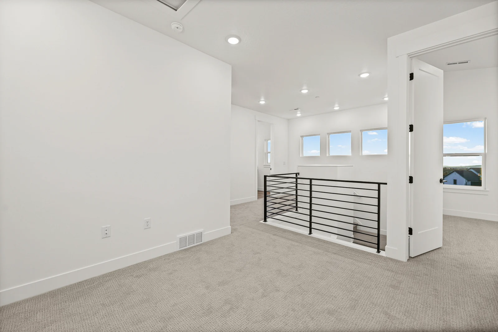 Carpeted upper-level loft with recessed lights, open stair railing, windows, and multiple doorways in Hawthorne Modern, Ogden.