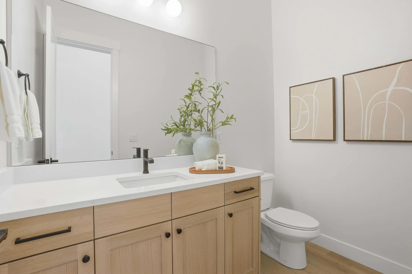 Compact powder room with a wood vanity, white countertop, round mirror, toilet, and bright white walls in the Denali model, American Fork.