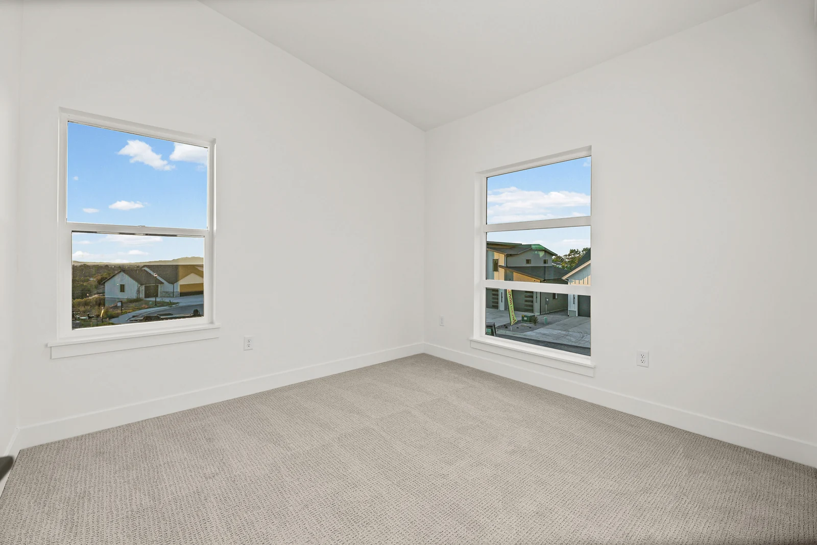 Unfurnished carpeted bedroom with two windows, white walls, and a view across nearby rooftops in Hawthorne Modern, Ogden.