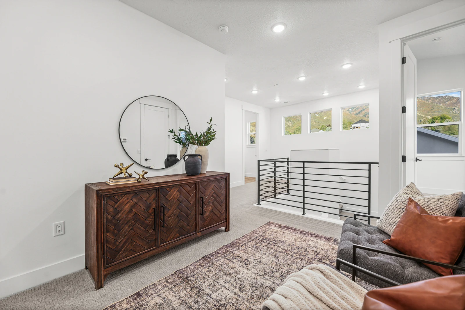 Upper landing includes a wood console, round mirror, seating, railing, and several windows in Hawthorne Farmhouse, Ogden.