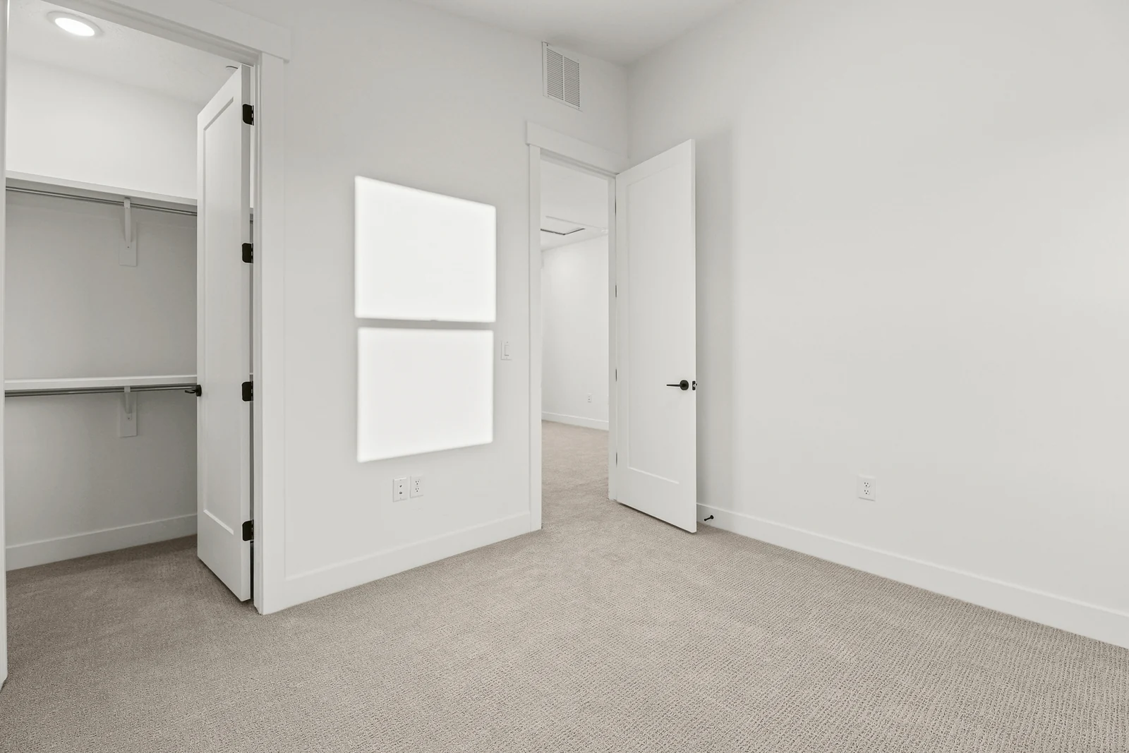 Unfurnished carpeted bedroom showing a window, open closet, white walls, and wood-trimmed door in Hawthorne Modern, Ogden.