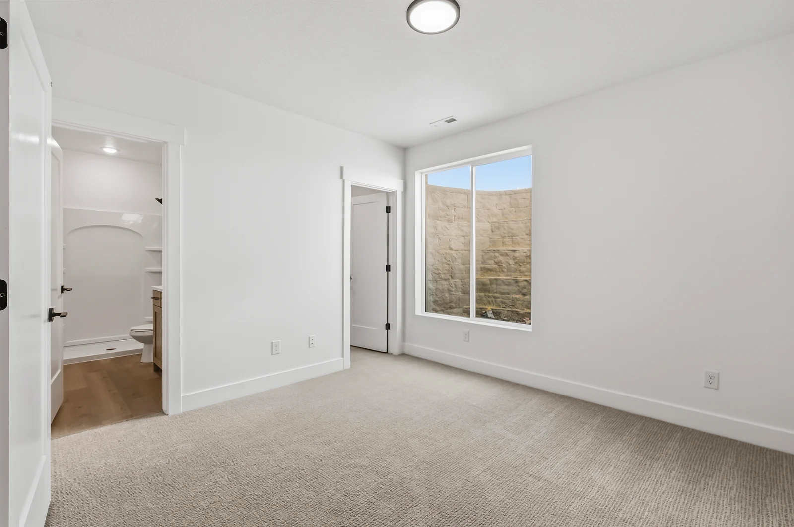 Carpeted lower-level bedroom with window, open doorway toward the bathroom, and bright white walls at Chestnut MW311, Stansbury Park.