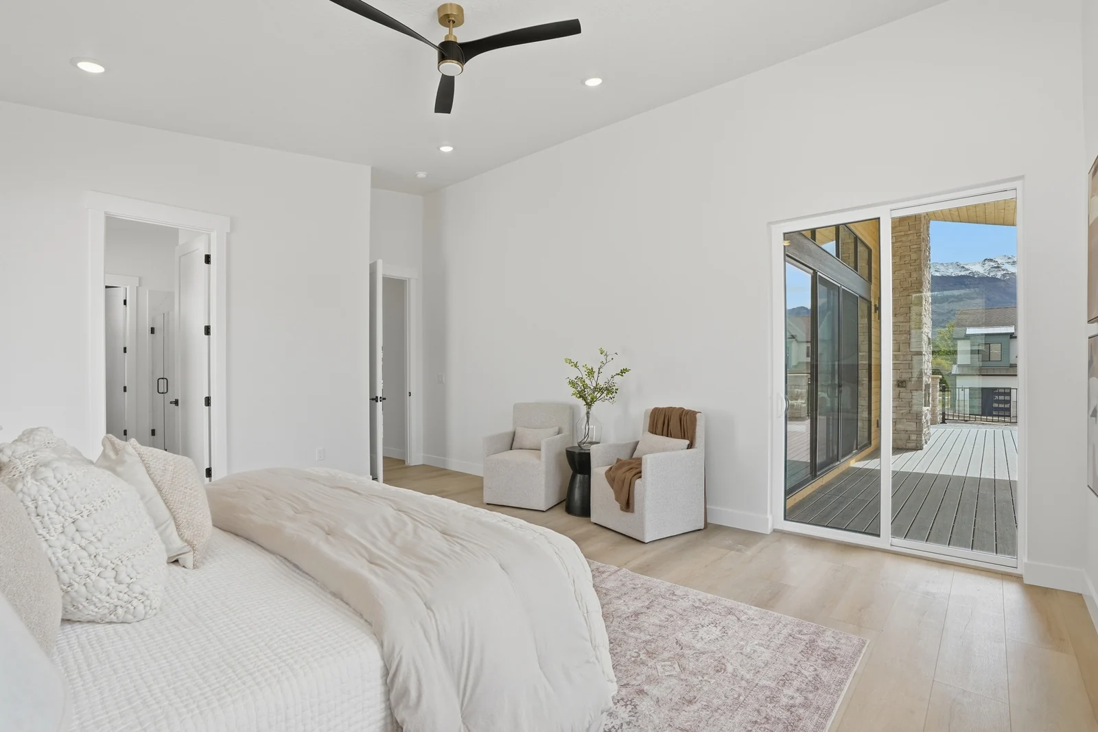 Bright bedroom with a made bed, lounge chair, ceiling fan, tall windows, and a glass door to an exterior space in the Denali model, American Fork.