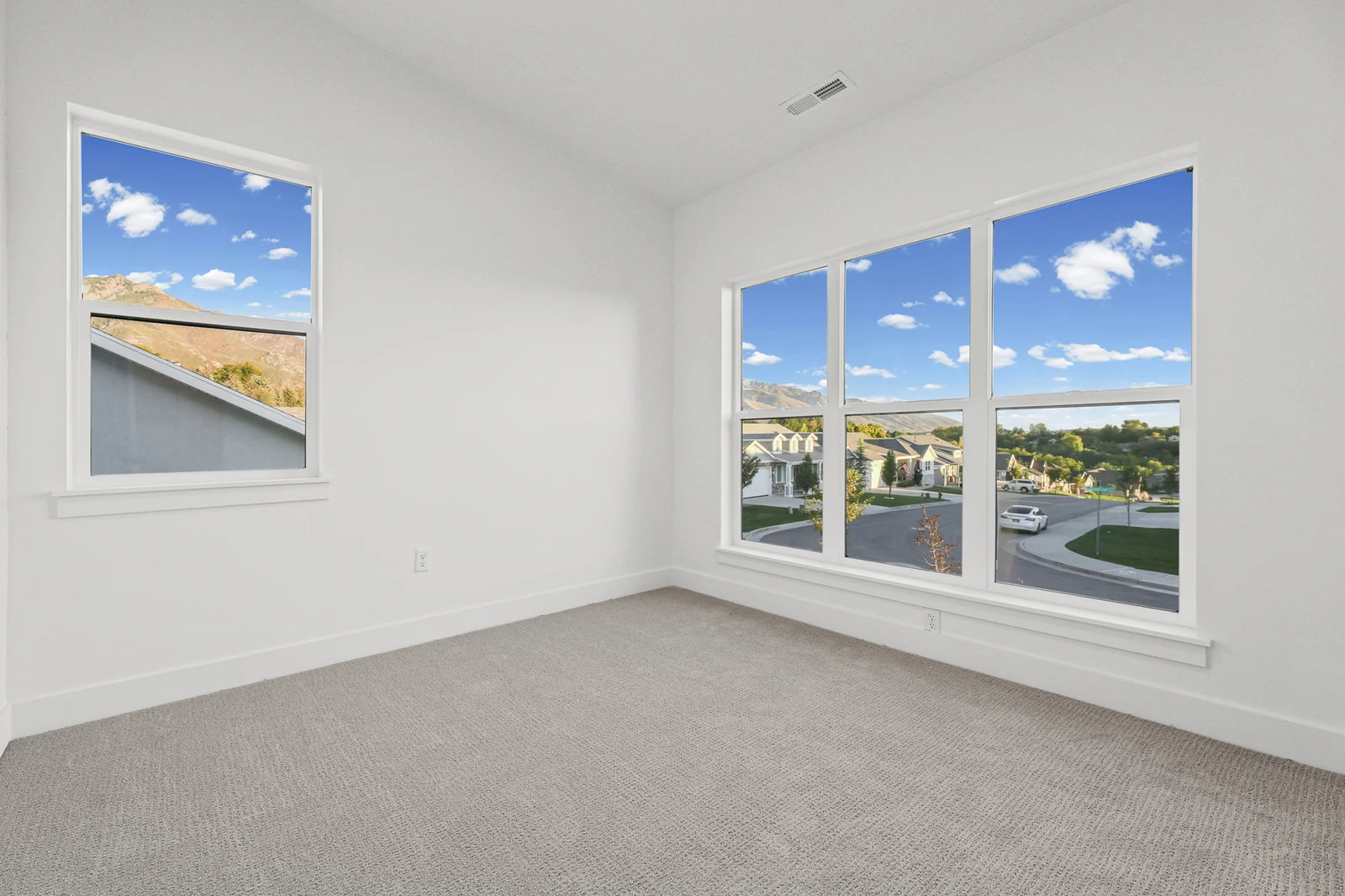 Unfurnished carpeted bedroom has a large corner window, white walls, and recessed lighting in Hawthorne Farmhouse, Ogden.