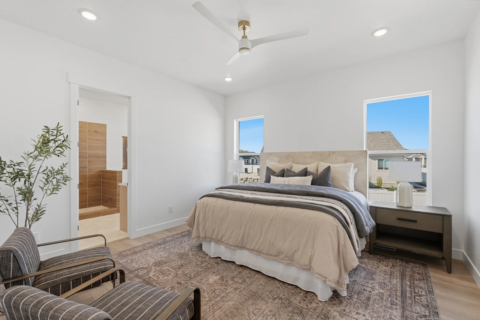 Staged bedroom with neutral bedding, ceiling fan, bedside tables, and windows facing the yard in Chestnut Modern MW302, Stansbury Park.