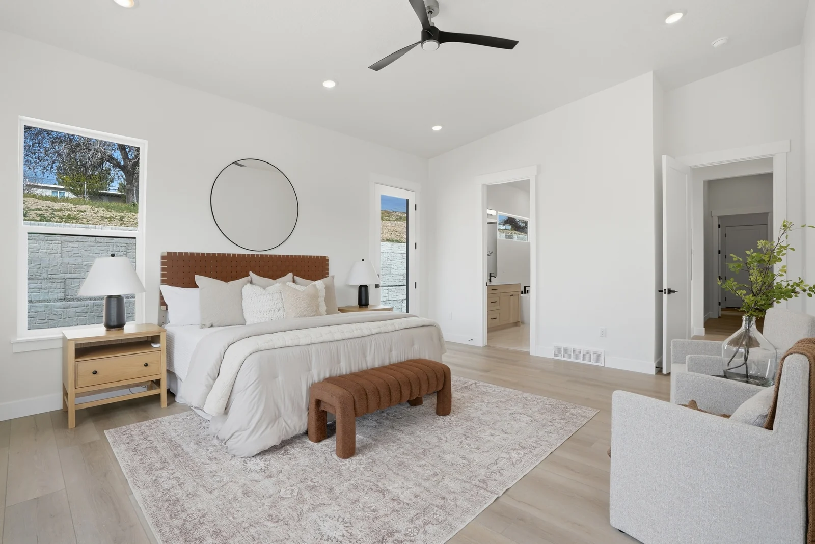 Bedroom overview with a wood bed frame, neutral seating, broad rug, recessed lights, and an open connection to the bathroom in the Denali model, American Fork.