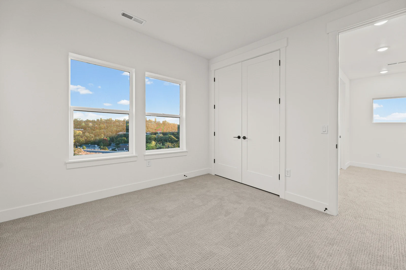 Unfurnished carpeted bedroom with two windows, double closet doors, and a white interior door in Hawthorne Modern, Ogden.