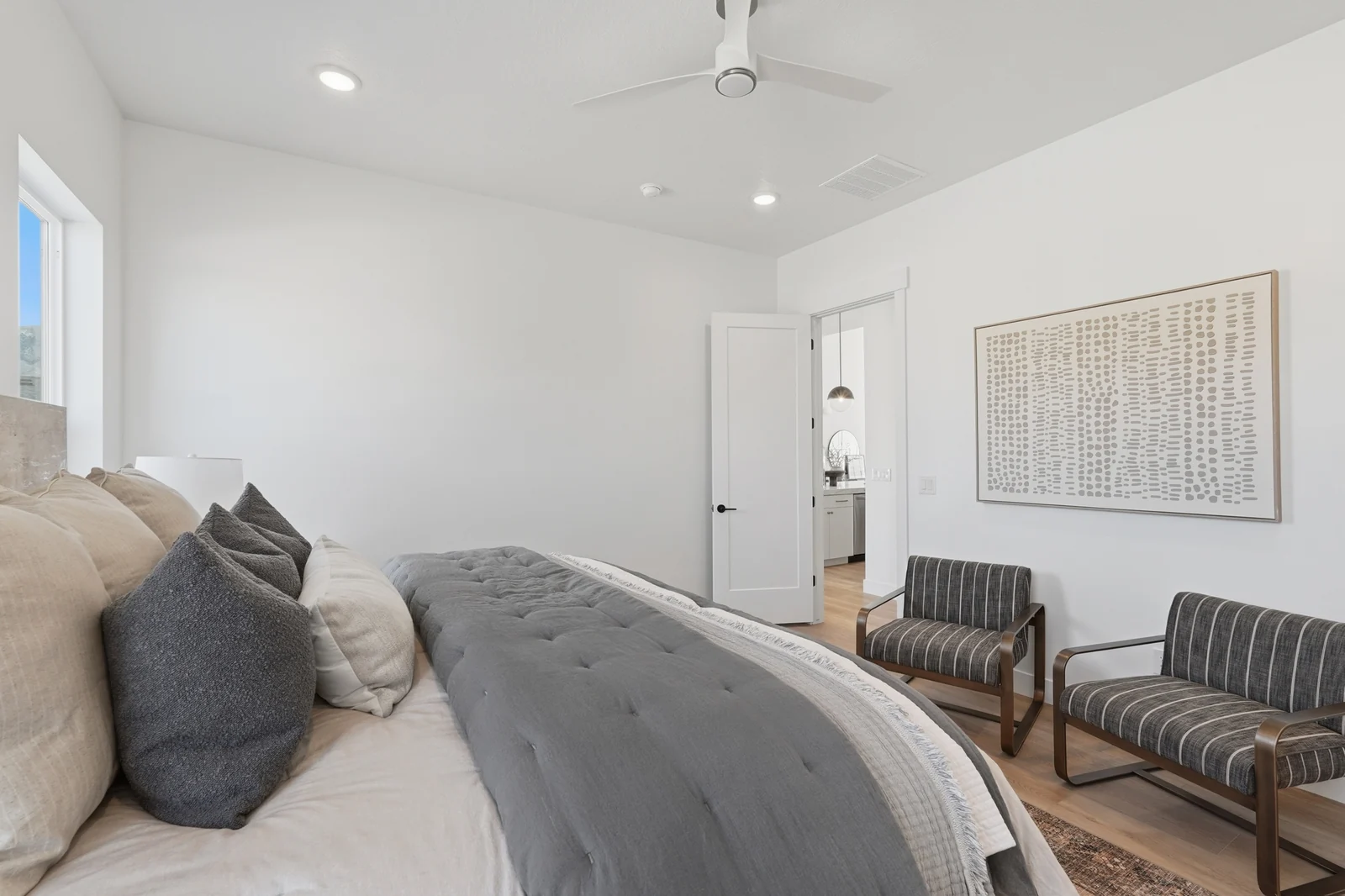 Wide bedroom view with a made bed, seating, ceiling fan, windows, and adjoining doorway in Chestnut Modern MW302, Stansbury Park.
