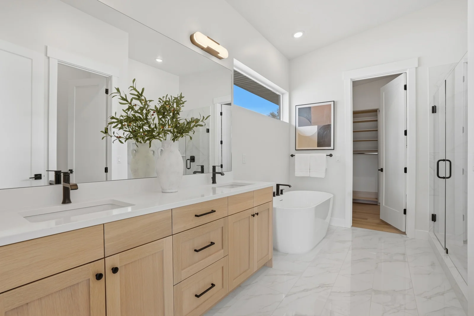 Large bathroom with double wood vanity, freestanding soaking tub, marble-look flooring, and a glass shower enclosure in the Denali model, American Fork.