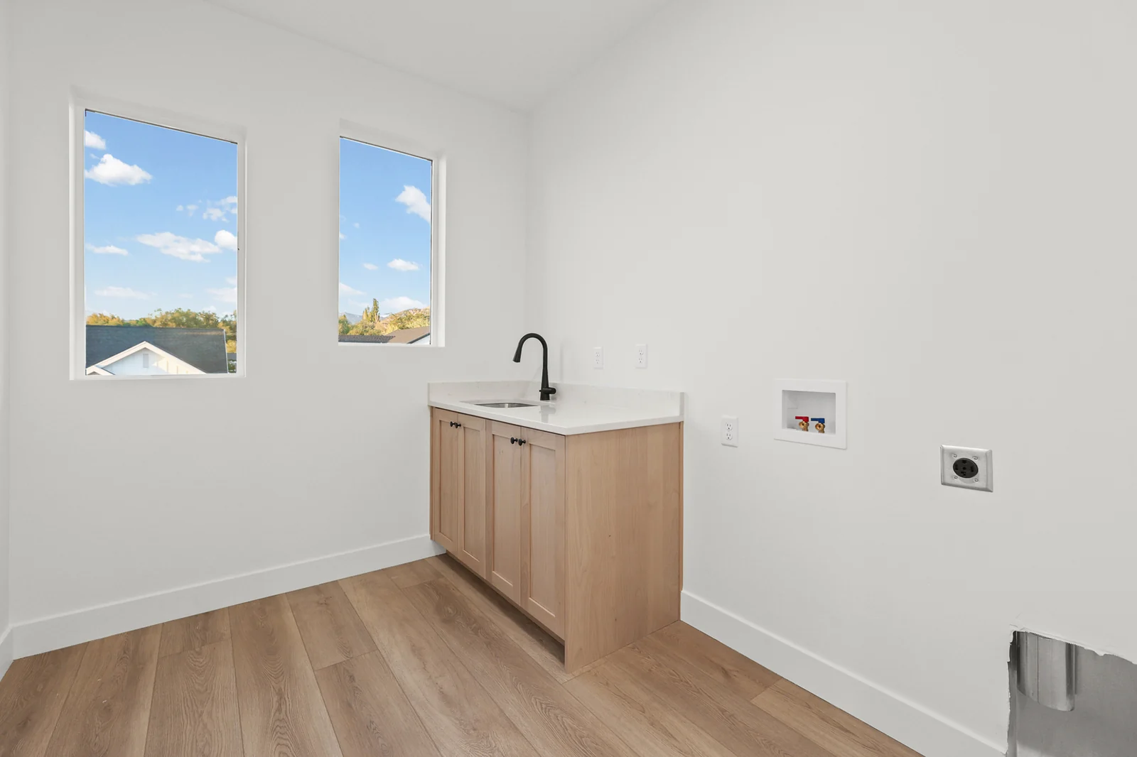 Laundry room with utility sink, wood cabinetry, appliance connections, high window, and wood-look flooring in Hawthorne Modern, Ogden.