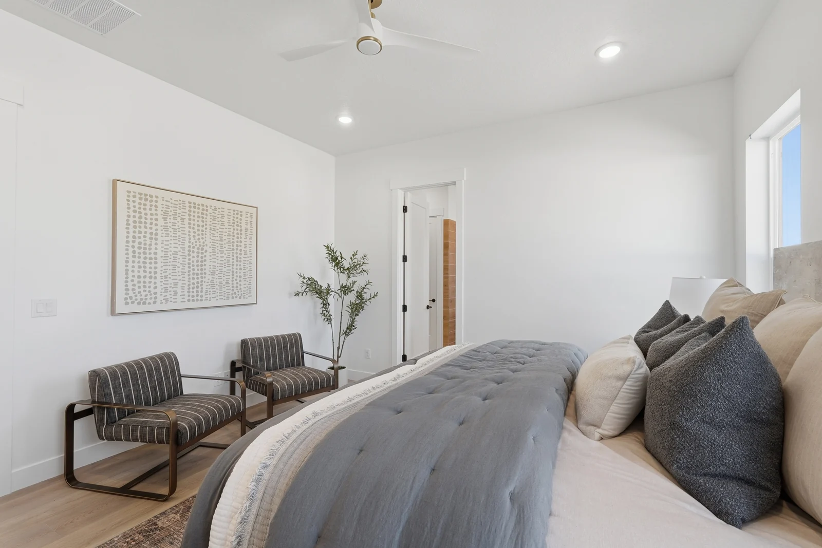 Bedroom perspective showing the bed, accent chairs, wall art, rug, and doorway in Chestnut Modern MW302, Stansbury Park.