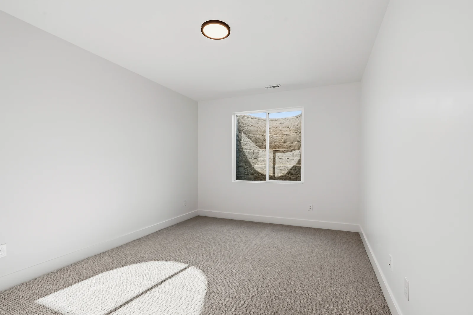 Empty carpeted lower-level bedroom with bright window, white walls, and simple ceiling light at Chestnut MW311, Stansbury Park.