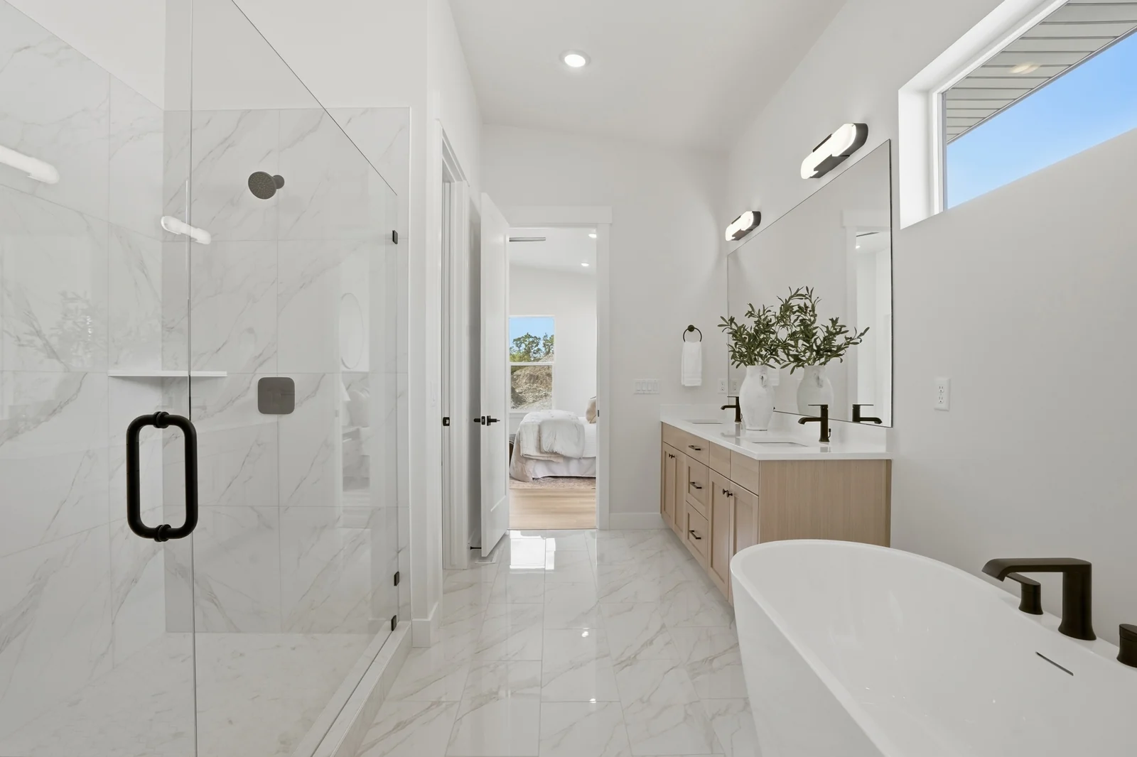 Bathroom featuring a freestanding tub, glass-enclosed shower, twin vanities, black fixtures, and marble-look floor tile in the Denali model, American Fork.