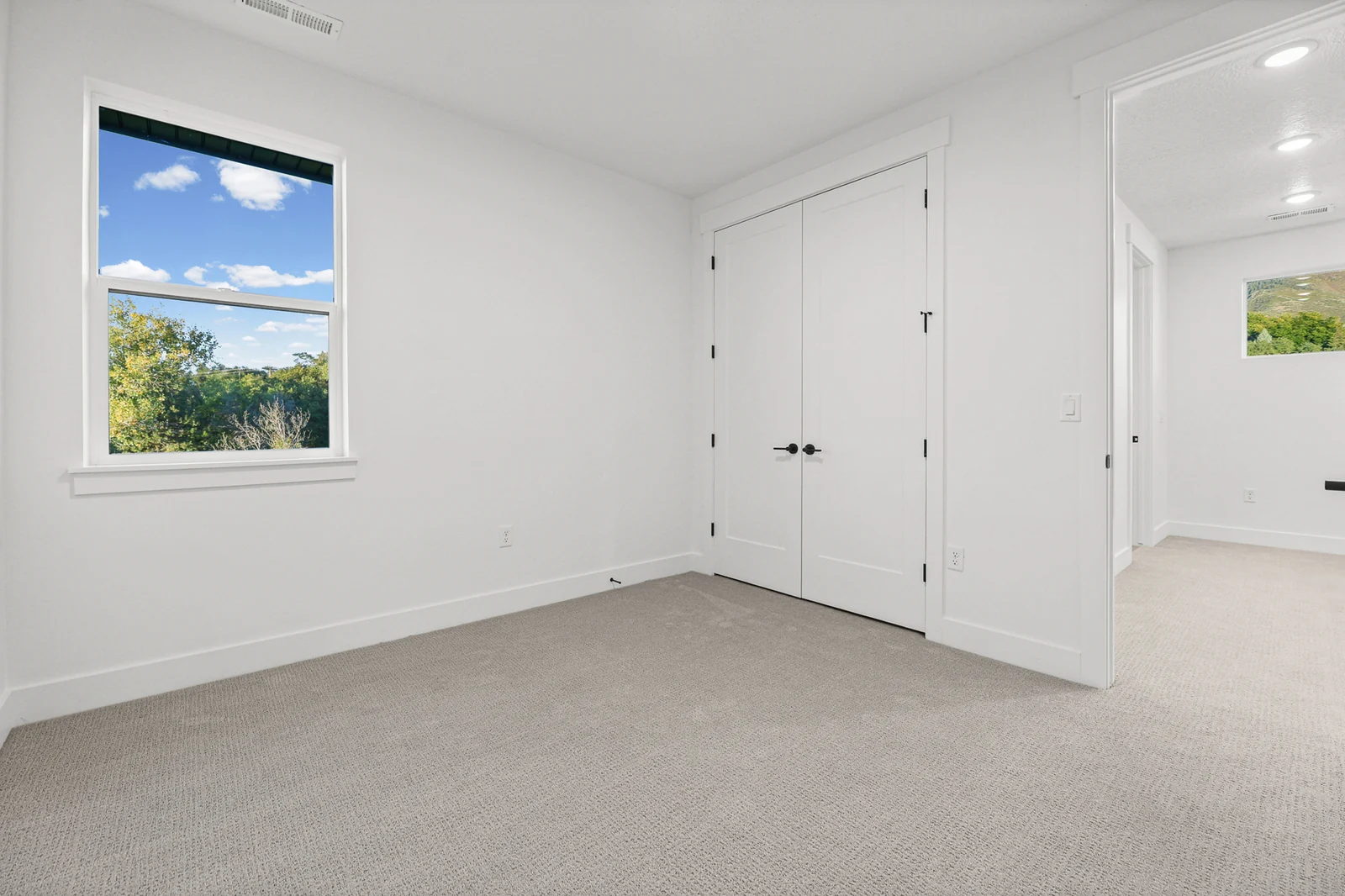 Carpeted bedroom includes double closet doors, a single window, and a wide white entry door in Hawthorne Farmhouse, Ogden.