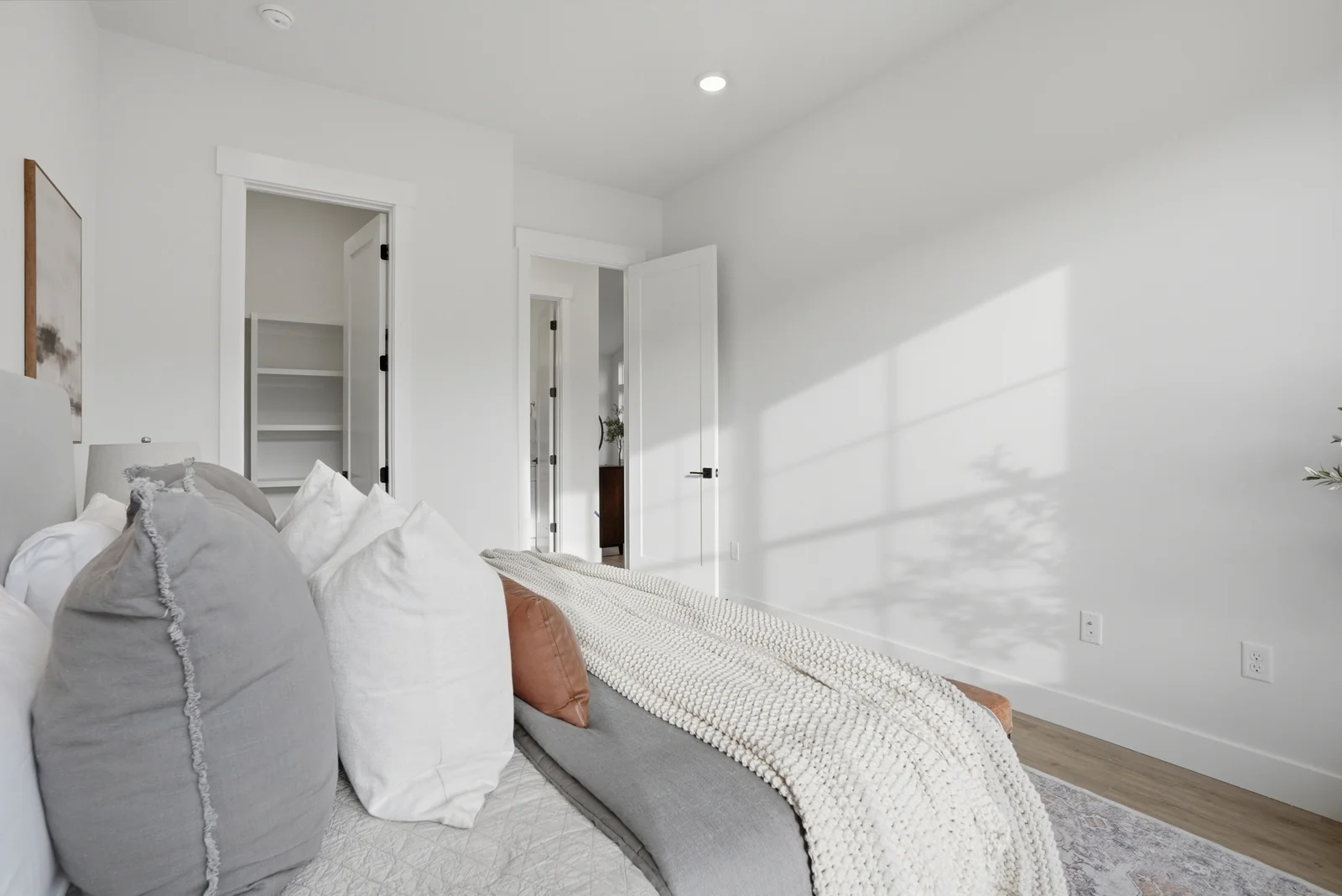 Staged bedroom with bed, bench, side table, window, and neutral carpet in Olympic BH08, American Fork.