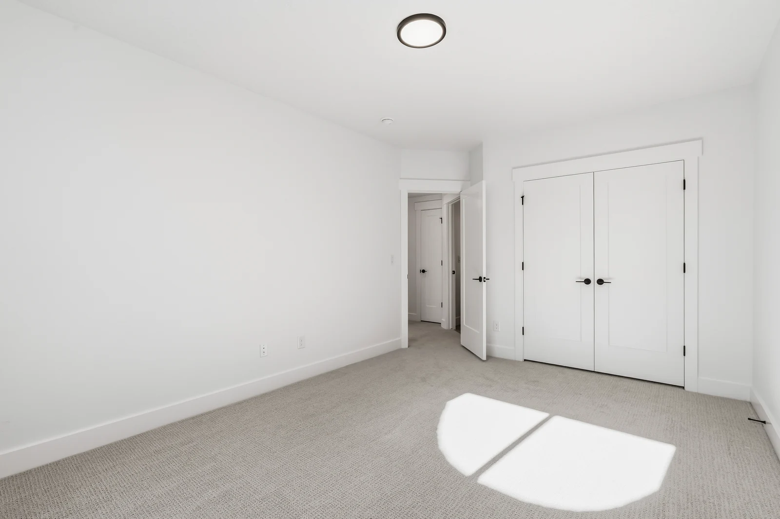 Empty carpeted lower-level bedroom with double closet doors, open doorway, and sunlight on the floor at Chestnut MW311, Stansbury Park.