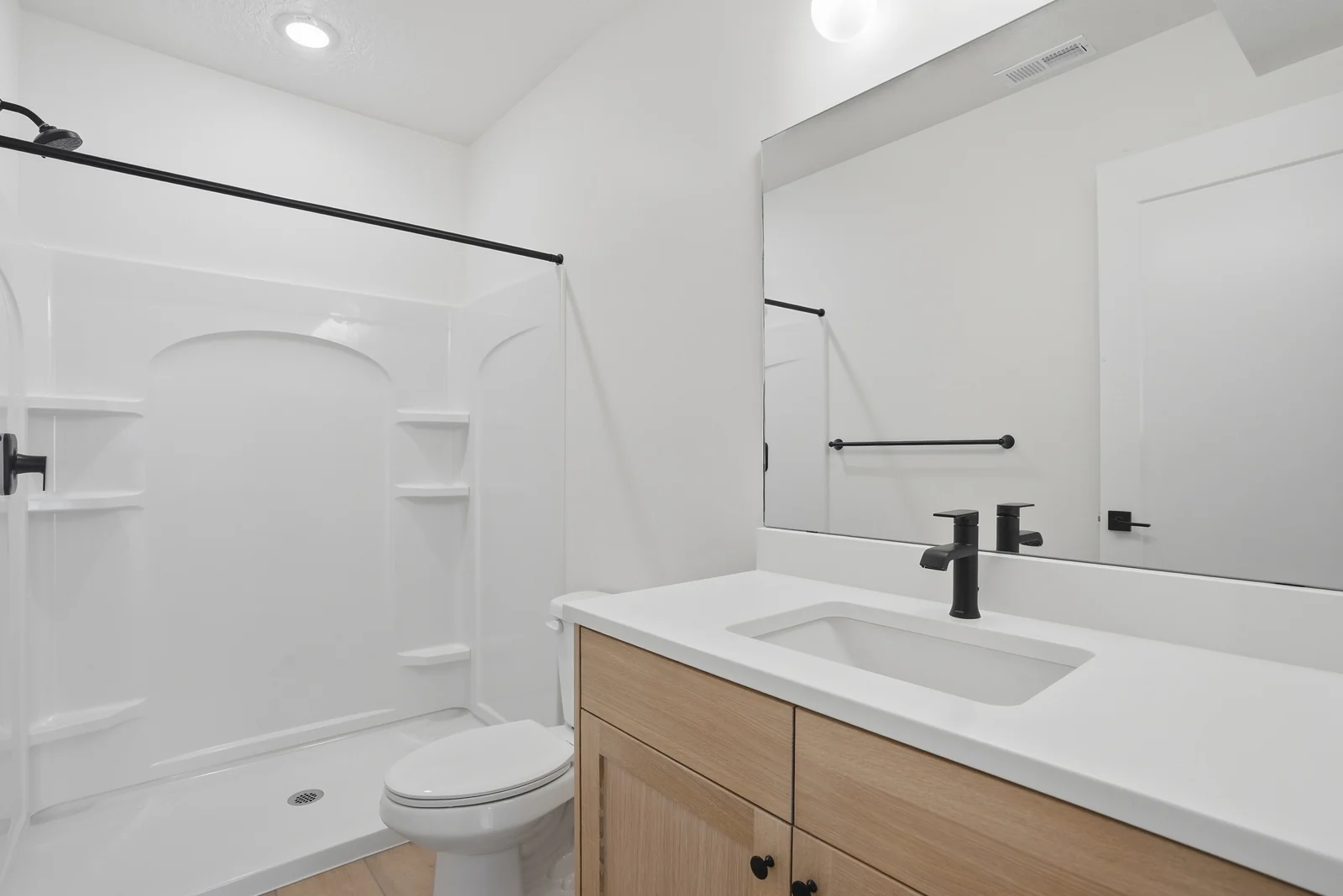 Bathroom with a single wood vanity, white countertop, toilet, and molded tub-shower combination beneath a dark rod in the Denali model, American Fork.