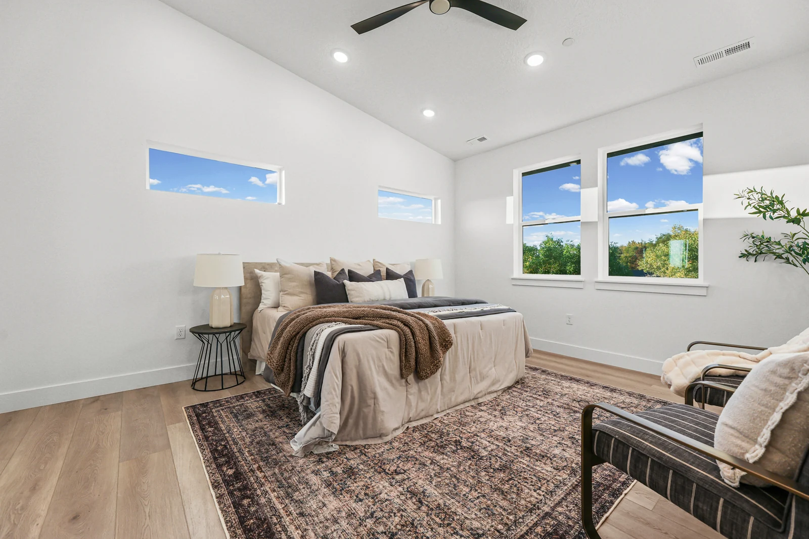 Staged bedroom includes a bed, accent chair, bench, rug, and bright corner windows in Hawthorne Farmhouse, Ogden.