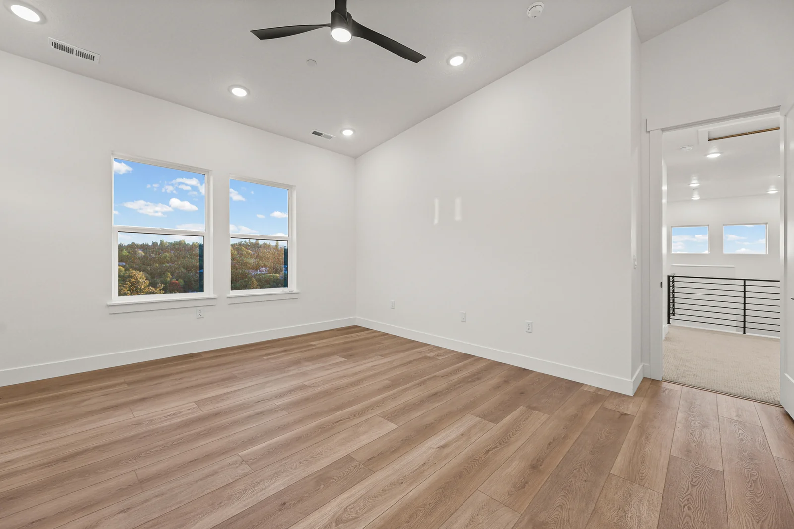 Unfurnished bedroom with wood-look flooring, ceiling fan, recessed lights, and windows overlooking the neighborhood in Hawthorne Modern, Ogden.